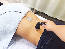 患者の腰に超音波・ハイボルテージコンビネーション治療器を当てるようす